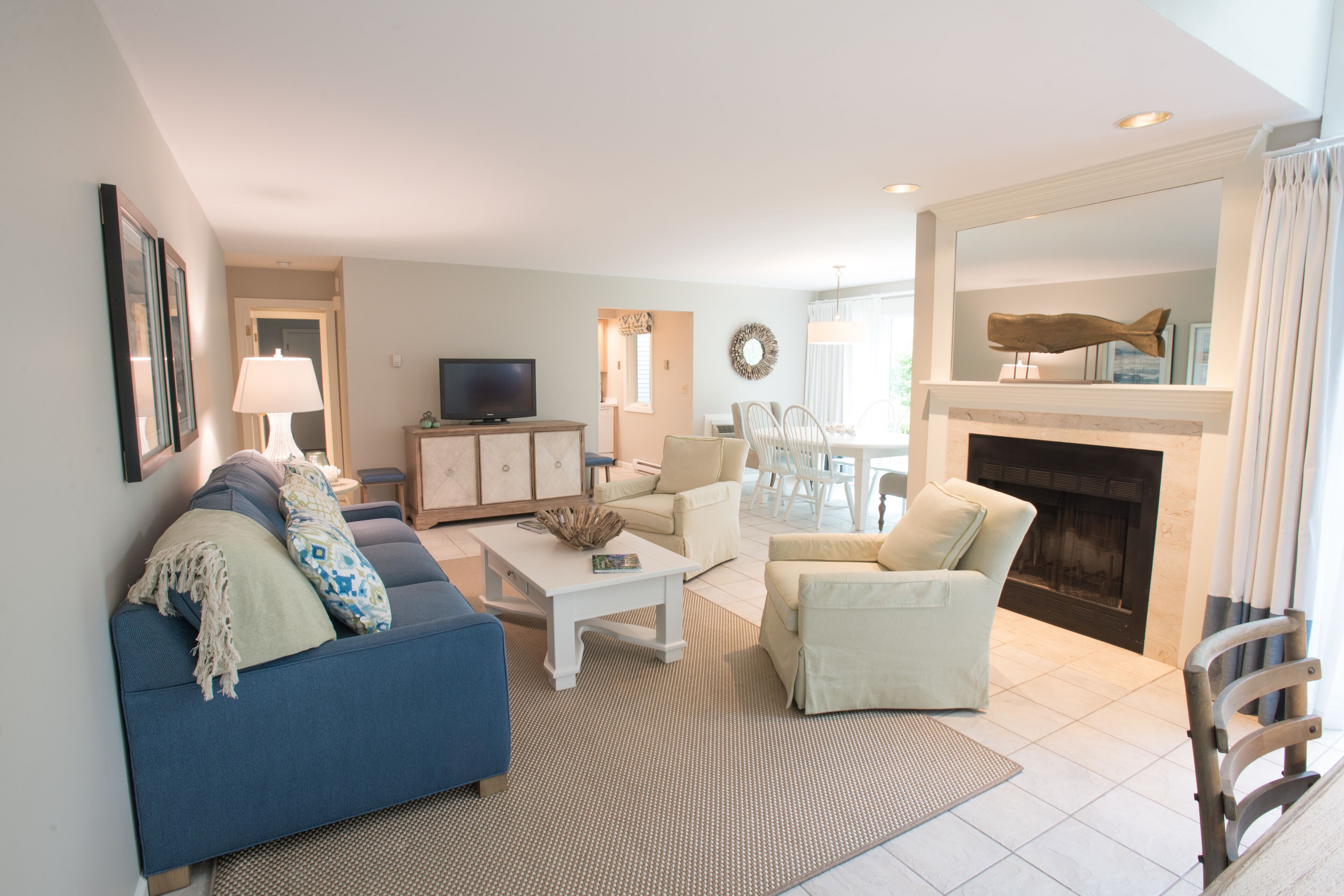 A living room with a blue sofa, white armchairs, a coffee table, and a fireplace.