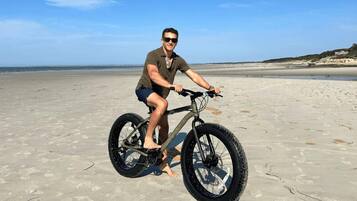 A person riding a bicycle on a sandy beach with the ocean in the background.