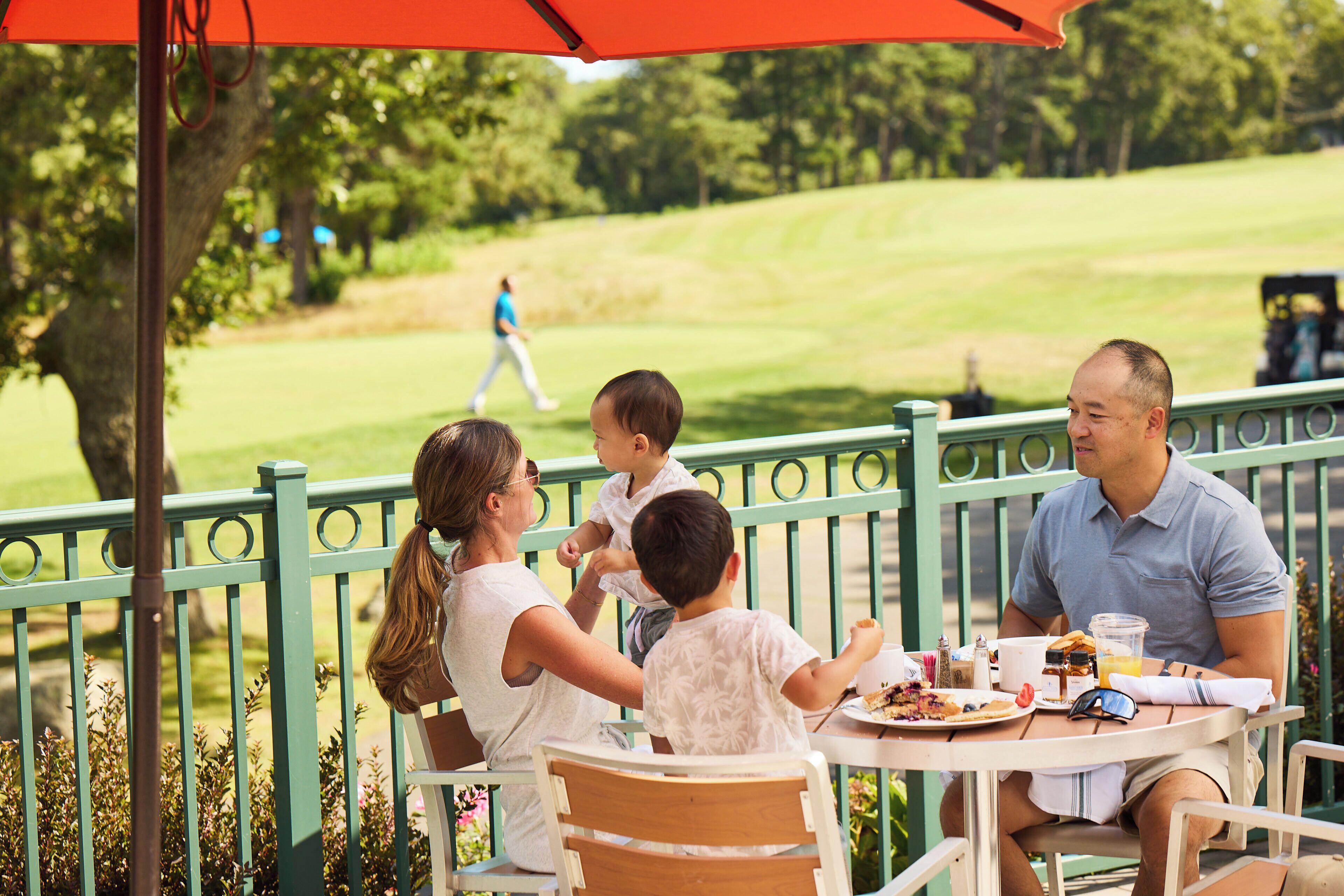 A family dining at an outdoor table with a view of a golf course.