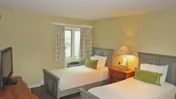 A room with two single beds, a bedside table with a lamp, a TV, and a window with curtains.