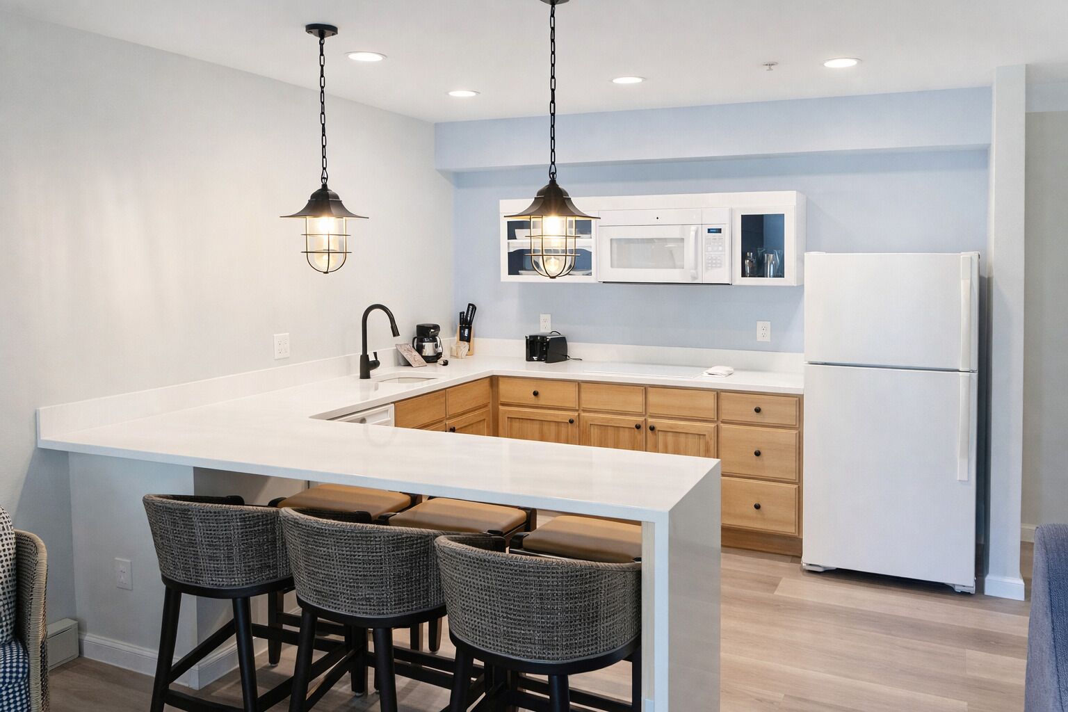 Una cocina moderna con una isla grande, armarios de madera, un refrigerador blanco e iluminación colgante.