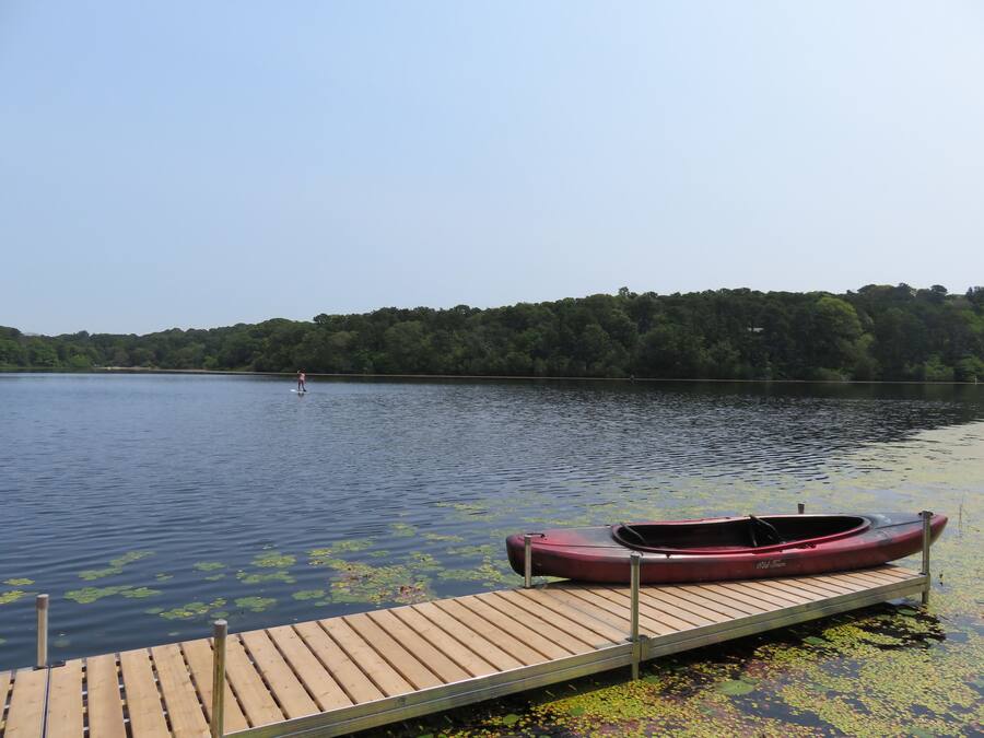 Un molo di legno con un canoa rossa, che si protende in acque calme con ninfee.