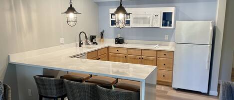 A modern kitchen with a large island, wooden cabinets, a white refrigerator, and pendant lighting.