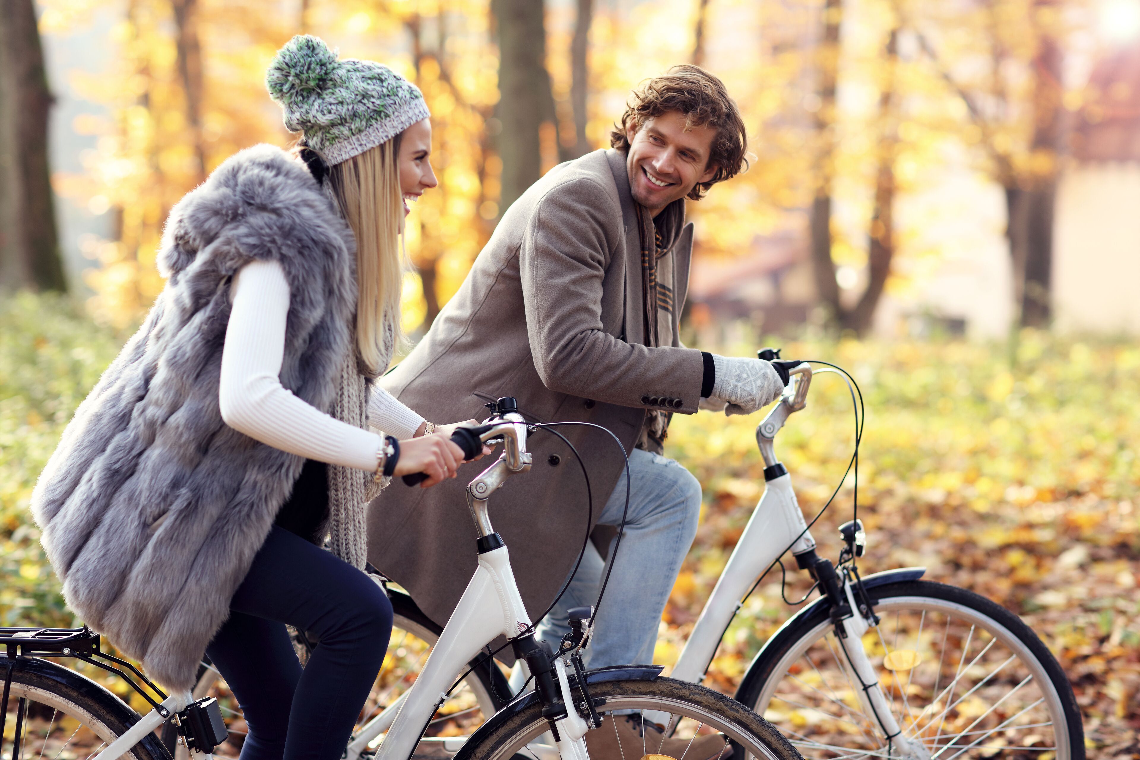 Two people on a bicycle in a park with autumn leaves.