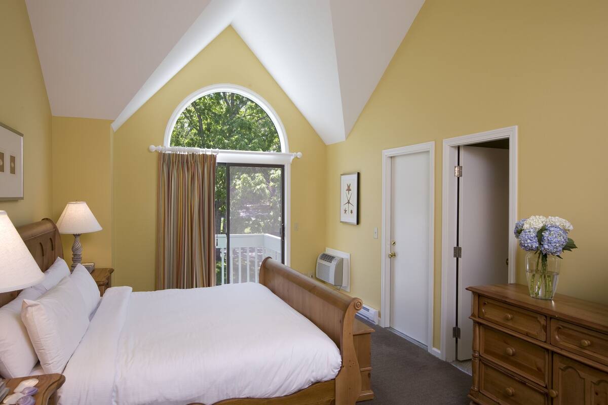 A bedroom with a large bed, a dresser, a window with curtains, and a door.
