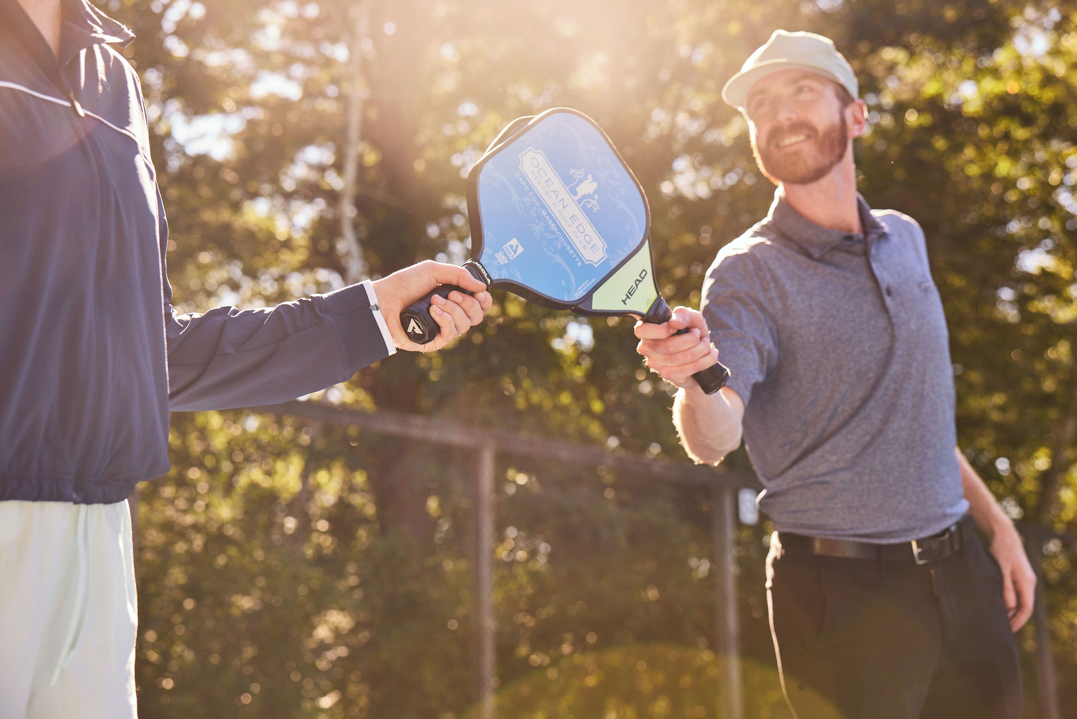 Two people holding a paddle, standing outdoors with trees in the background.