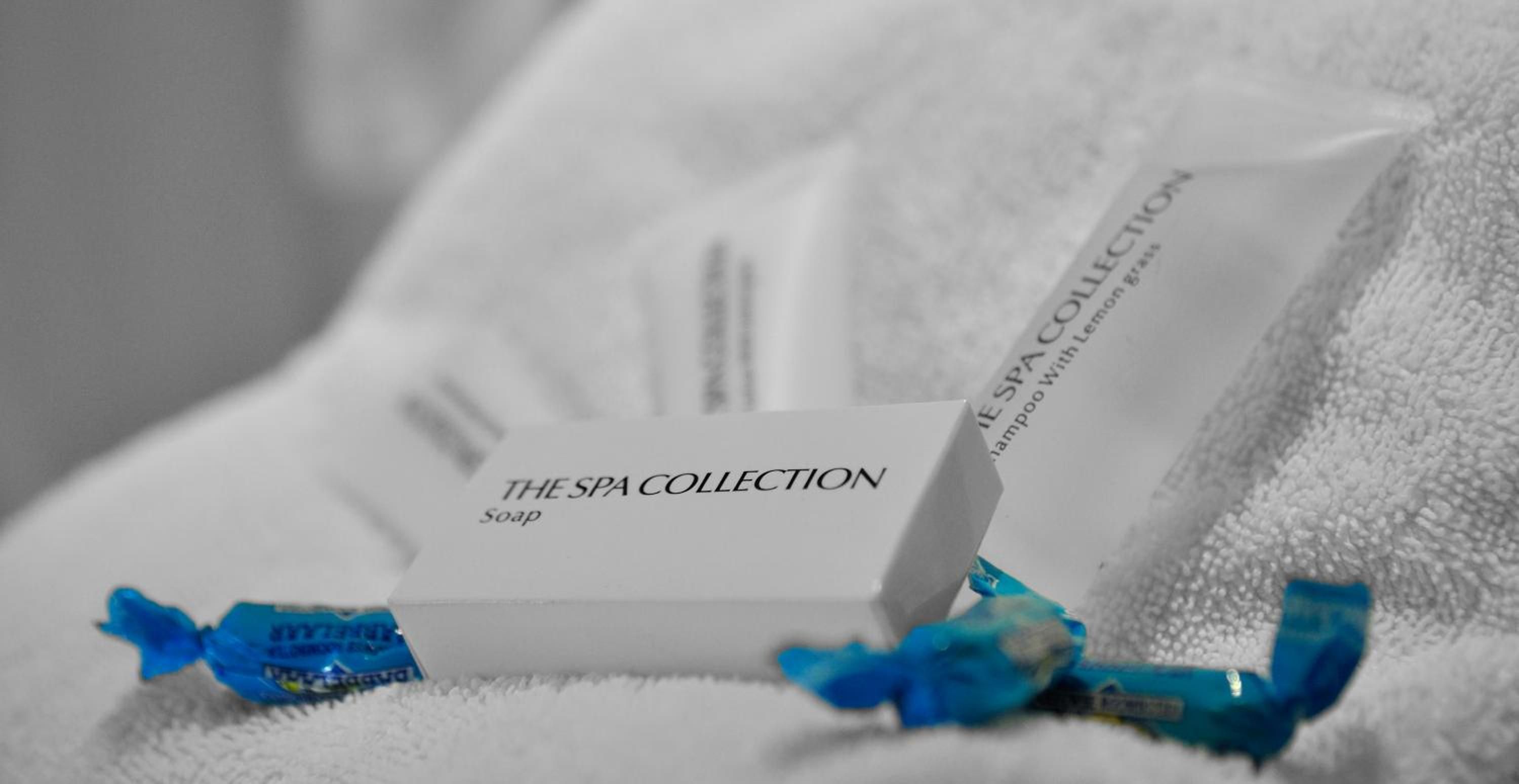 Een pakket met de aanduiding 'THE SPA COLLECTION', voorzien van een blauw lint, ligt op een witte handdoek.
