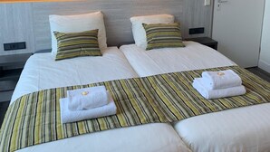Habitación de hotel con una cama grande, dos mesitas de noche, un armario y luces fijadas a la pared.