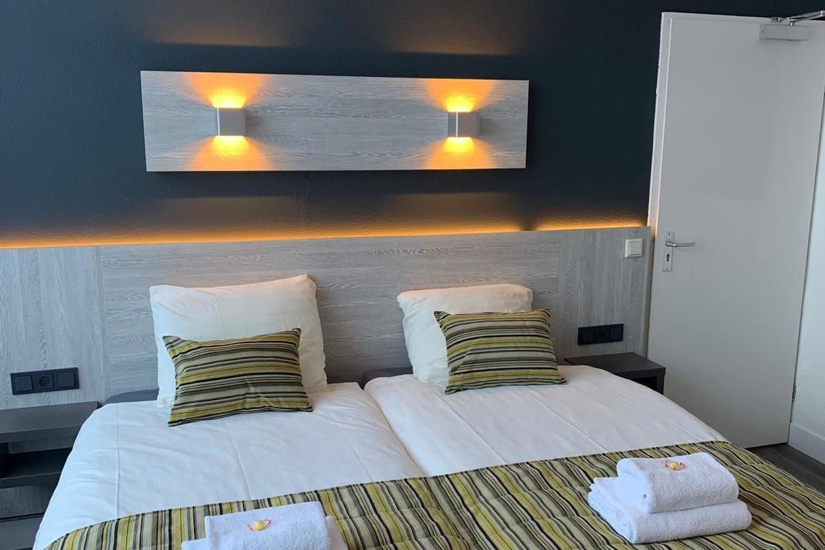 A hotel room with a large bed, two bedside tables, a wardrobe, and wall-mounted lighting.