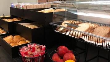 A breakfast buffet with bread, pastries, and fruits like apples and oranges.