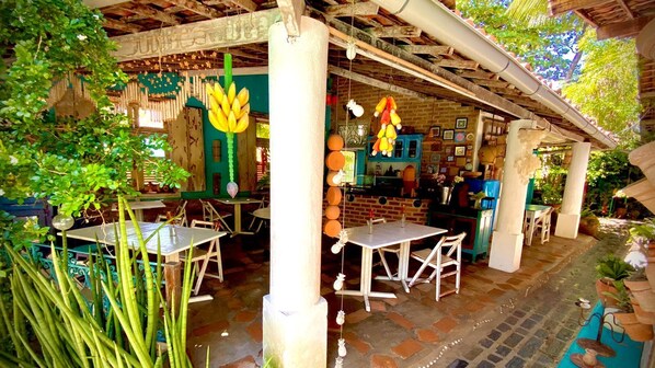 An outdoor dining area with tables and chairs, surrounded by plants and columns. - Pousada Porto Verde (Ipojuca)