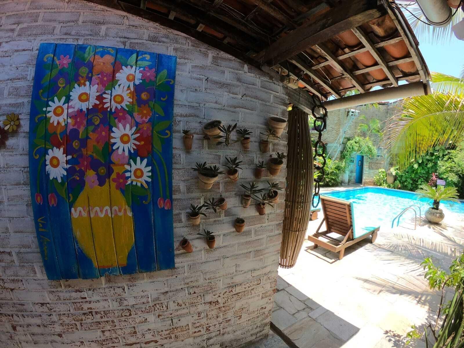 A rustic outdoor area with a brick wall, a colorful floral painting, and a variety of potted plants.