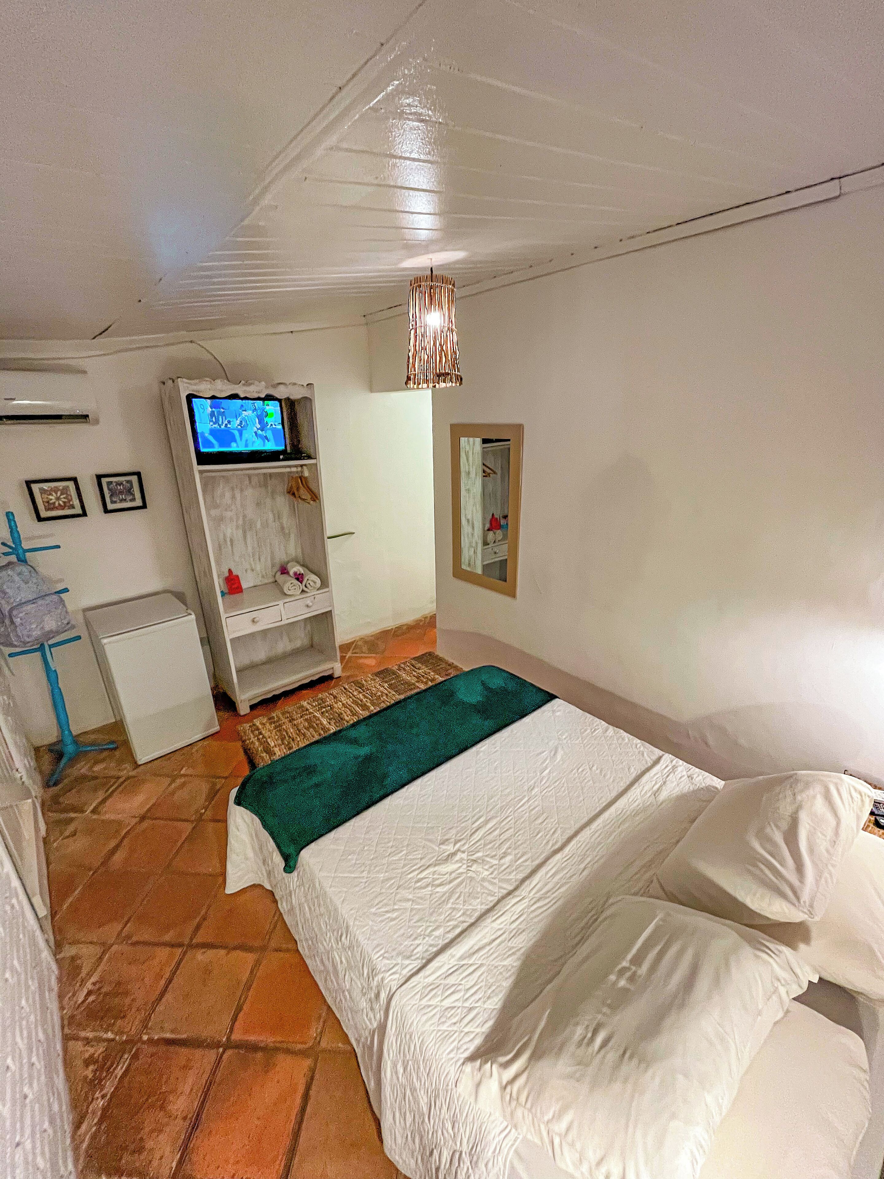 A bedroom with a bed, a TV on a stand, a wardrobe, and a mirror on the wall.