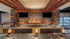 A bar area with copper pipes, a stone wall, and a variety of bottles and glasses. - The Wildbirch Hotel - JDV by Hyatt (Anchorage)
