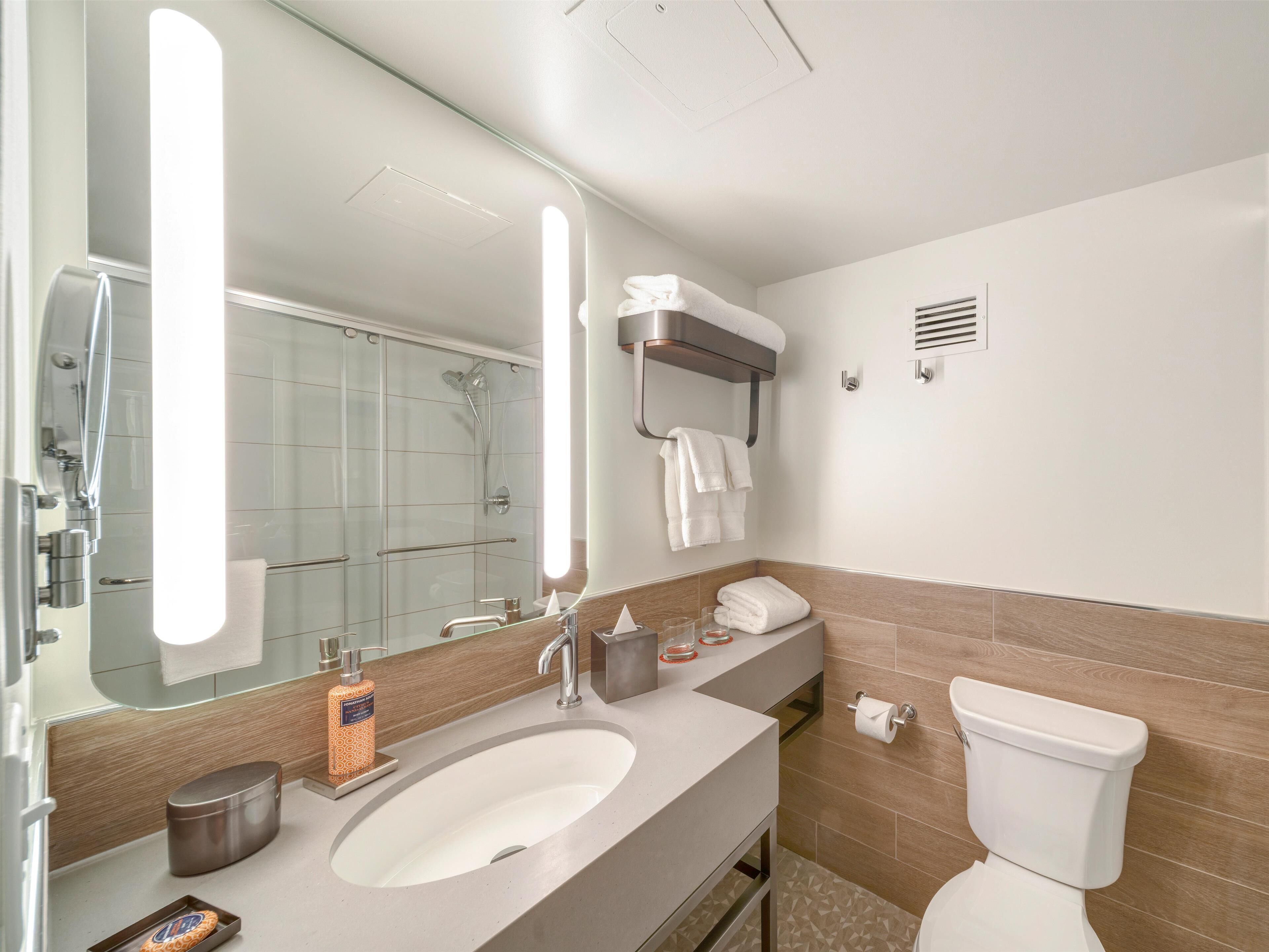 A modern bathroom with a large mirror, a sink, a toilet, and a shower area.