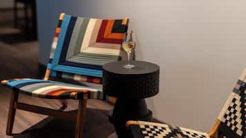 Quarto moderno com cadeira de madeira, poltrona estampada e pequena mesa com um copo de vinho.