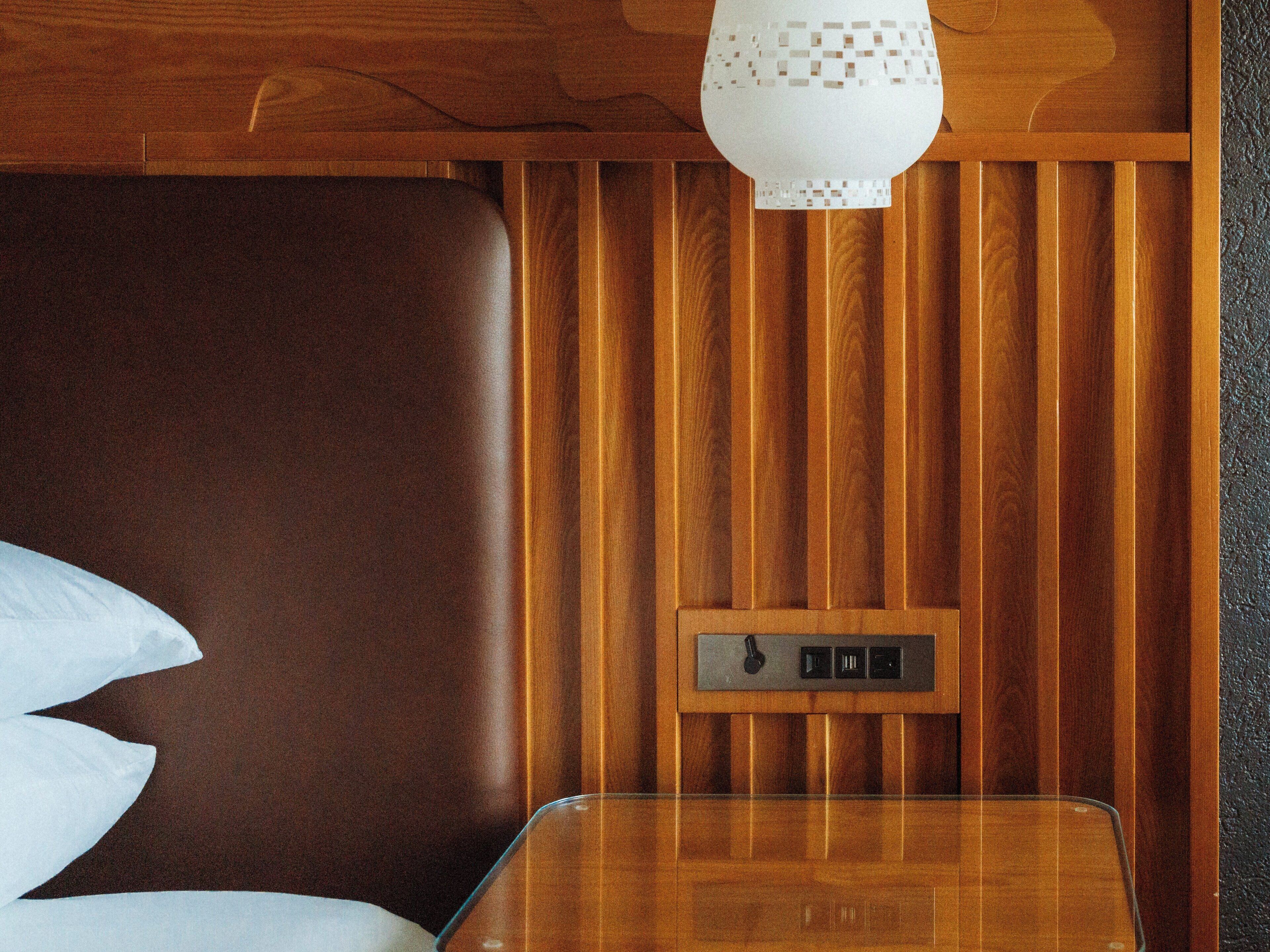 A wooden panel wall with a control panel, a leather headboard, and a glass table.