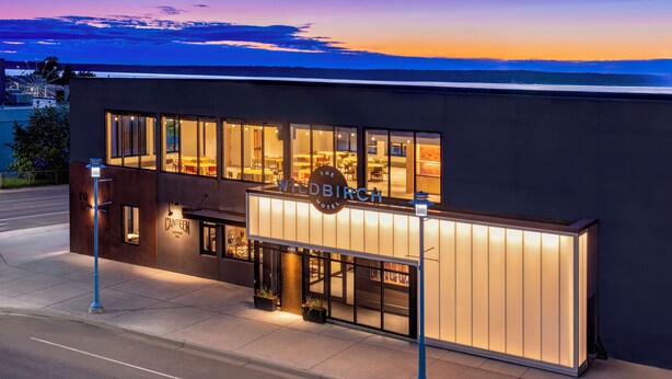 A modern hotel with a large illuminated sign, a visible restaurant named "Canteen Coffee," and a view of the sunset over the water. - The Wildbirch Hotel - JDV by Hyatt (Anchorage)
