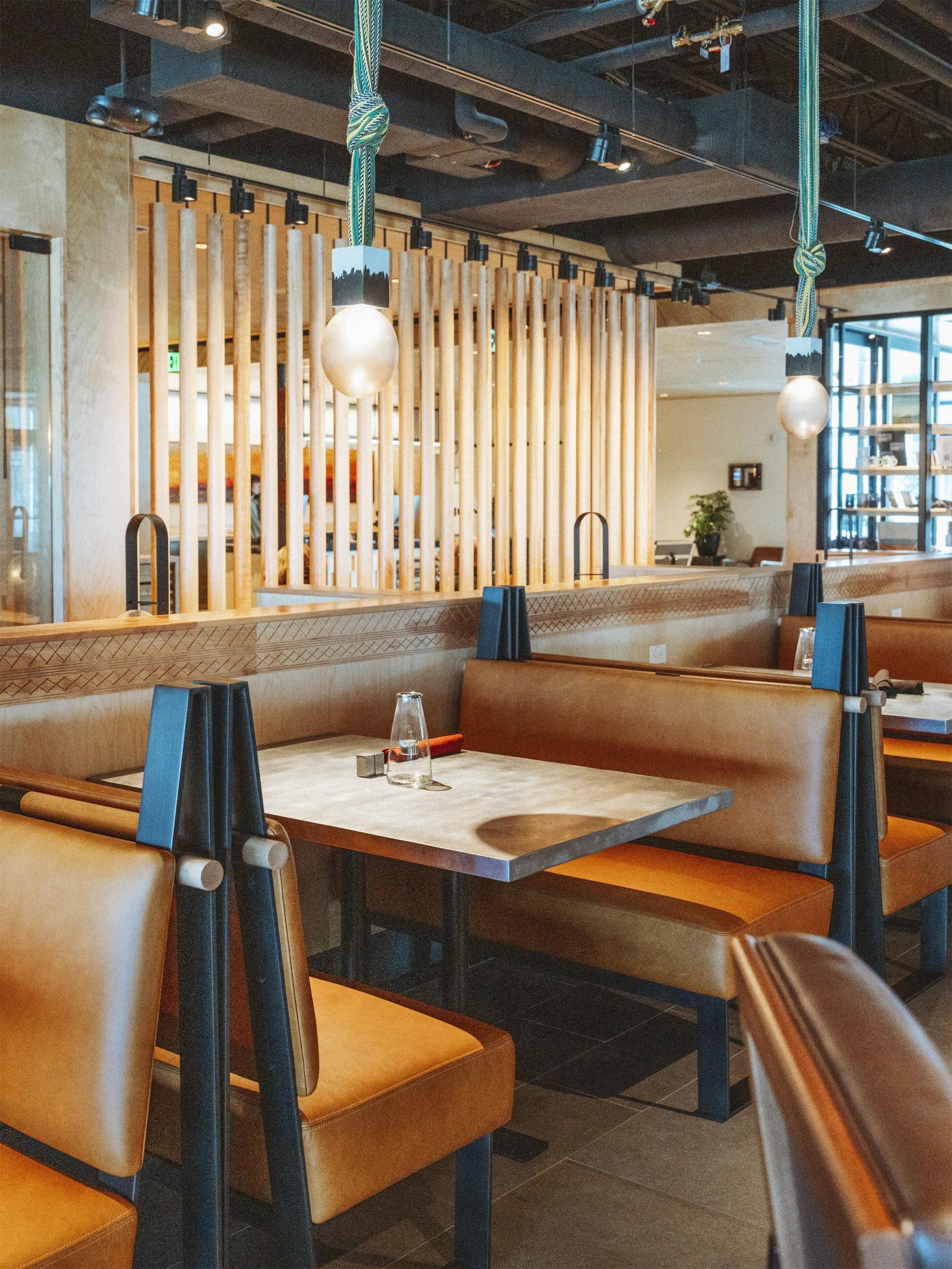 Un interior de restaurante con asientos tipo cabina, lámparas colgantes y un tabique de madera.