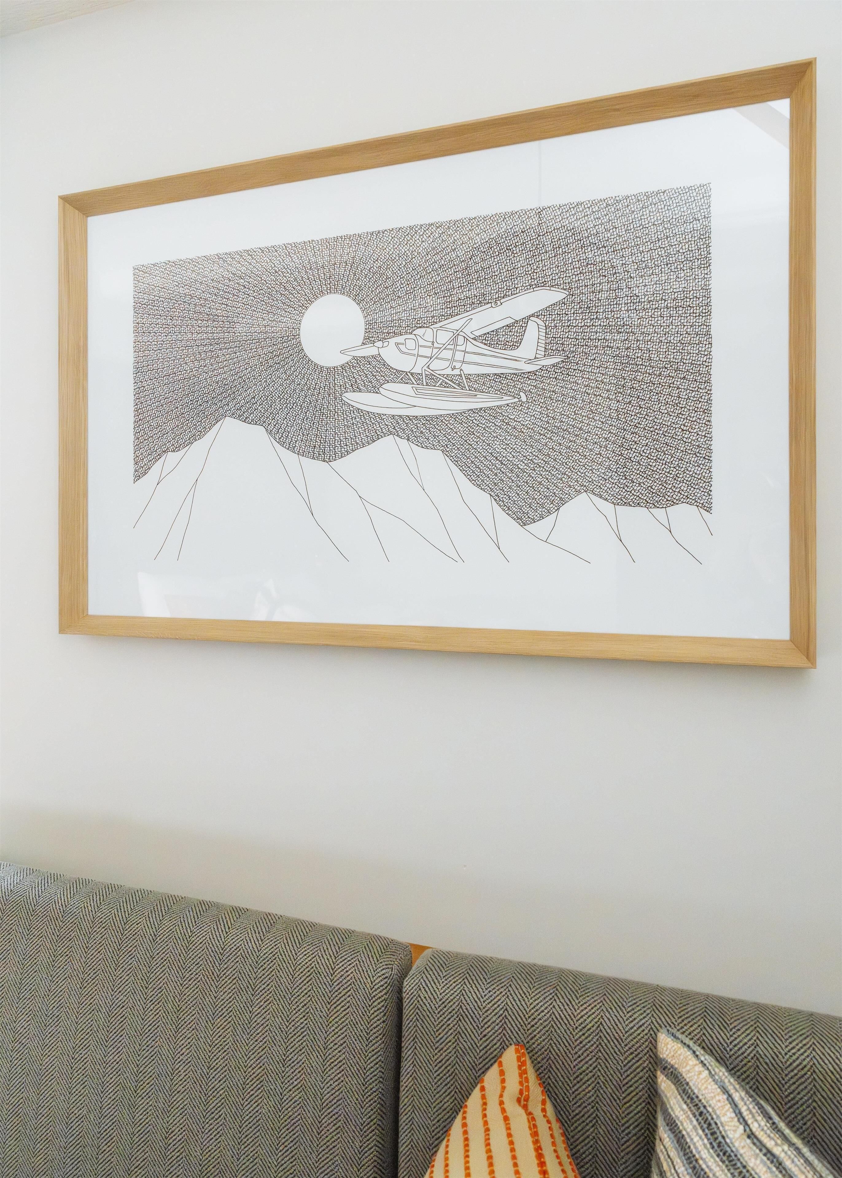 A framed artwork depicting a vintage aircraft flying over a mountainous landscape with a moon in the sky.