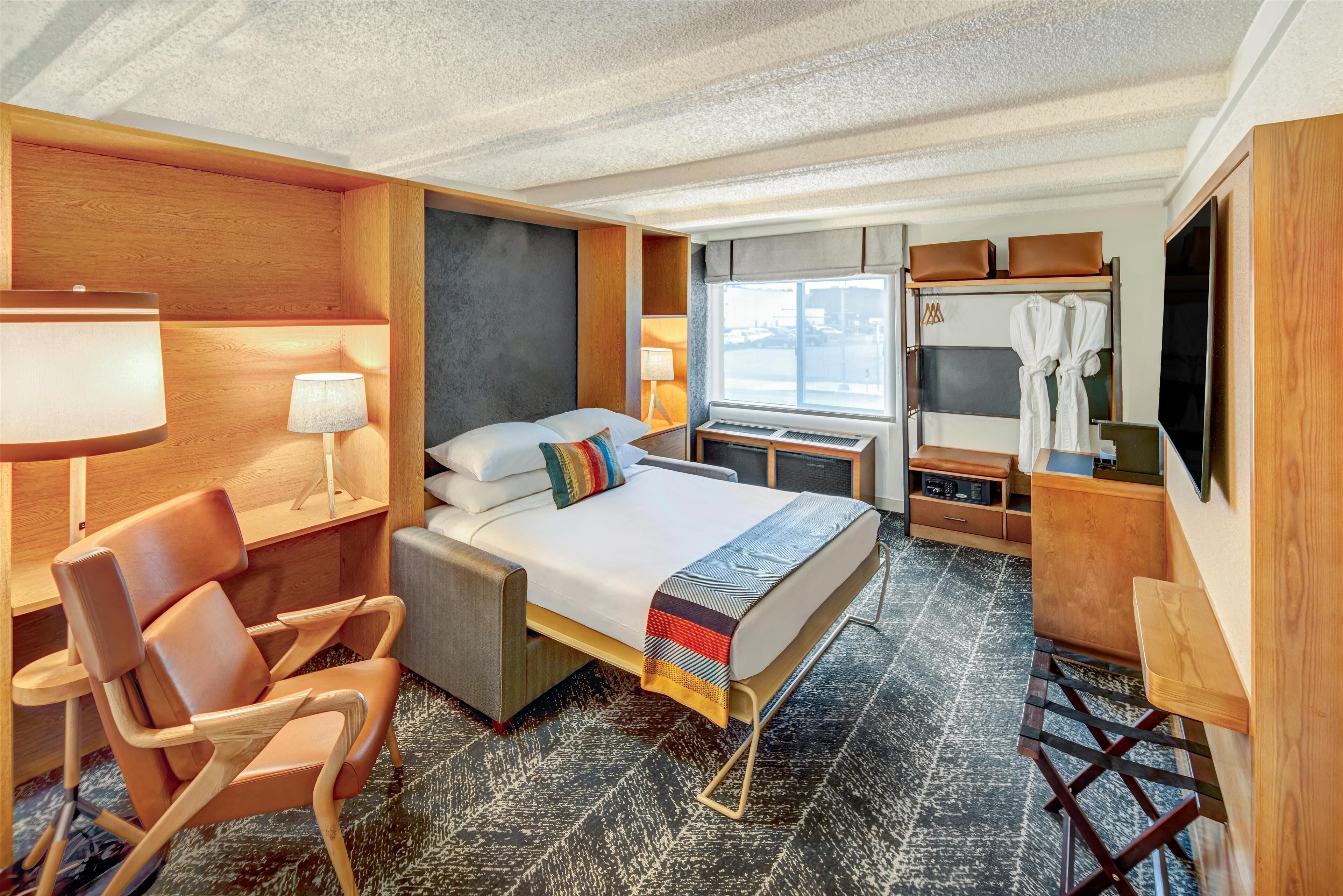 A hotel room with a bed, a chair, a desk, a TV, and a wardrobe.