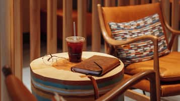 A round wooden table with a striped cushion, a drink with a straw, and a closed notebook.