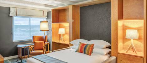 A hotel room with a large bed, two bedside tables with lamps, a chair, and a view of the city through the window.
