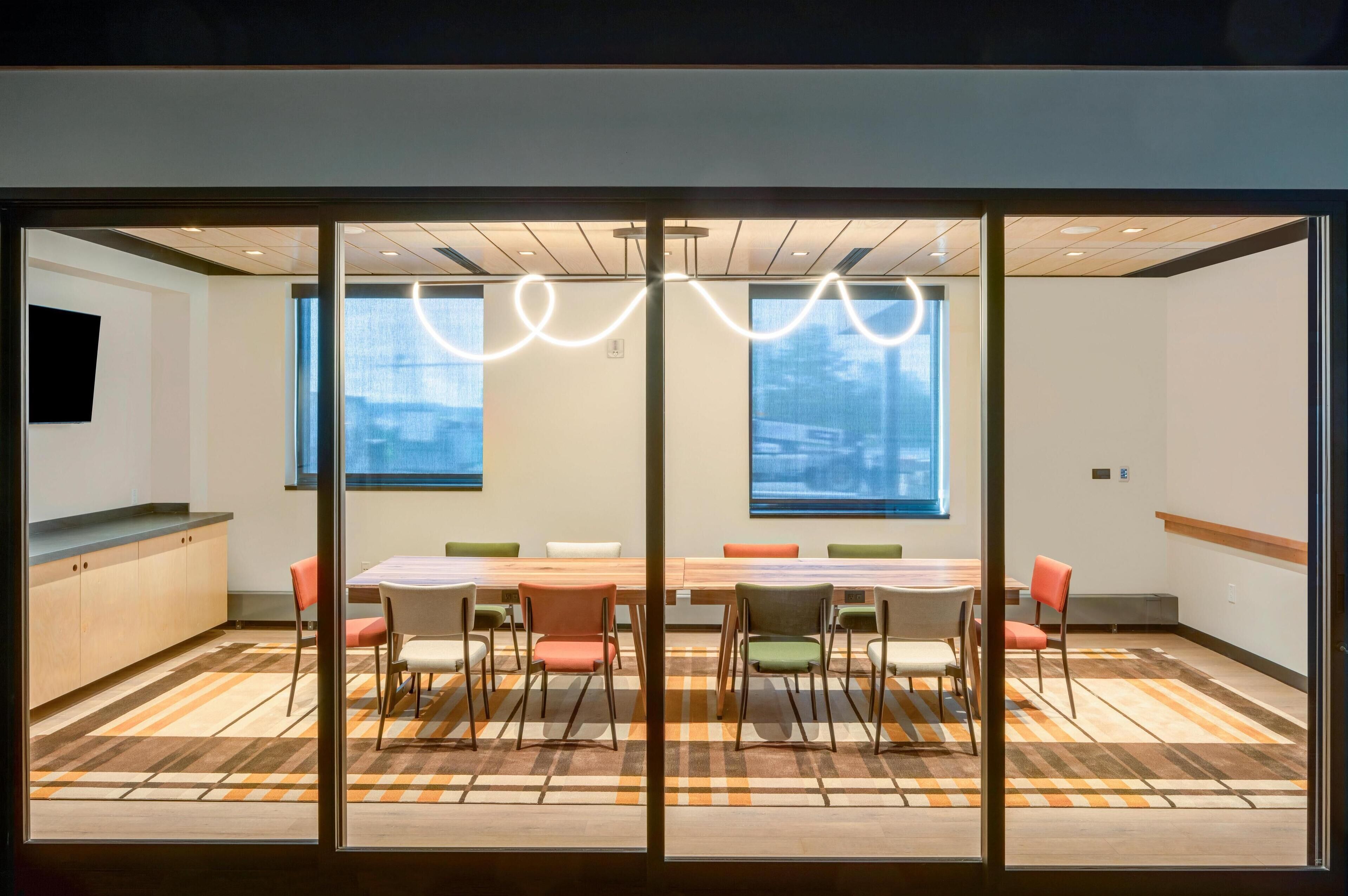 A modern meeting room with a large table, colorful chairs, and large windows with a view.