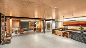 A spacious lobby with a wooden ceiling, a reception desk, seating area, and a fireplace. - The Wildbirch Hotel - JDV by Hyatt (Anchorage)