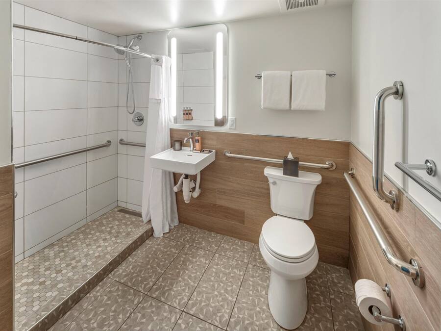 Een moderne badkamer met douche, toilet en wastafel. Er zijn handgrepen en een handrail voor toegankelijkheid.