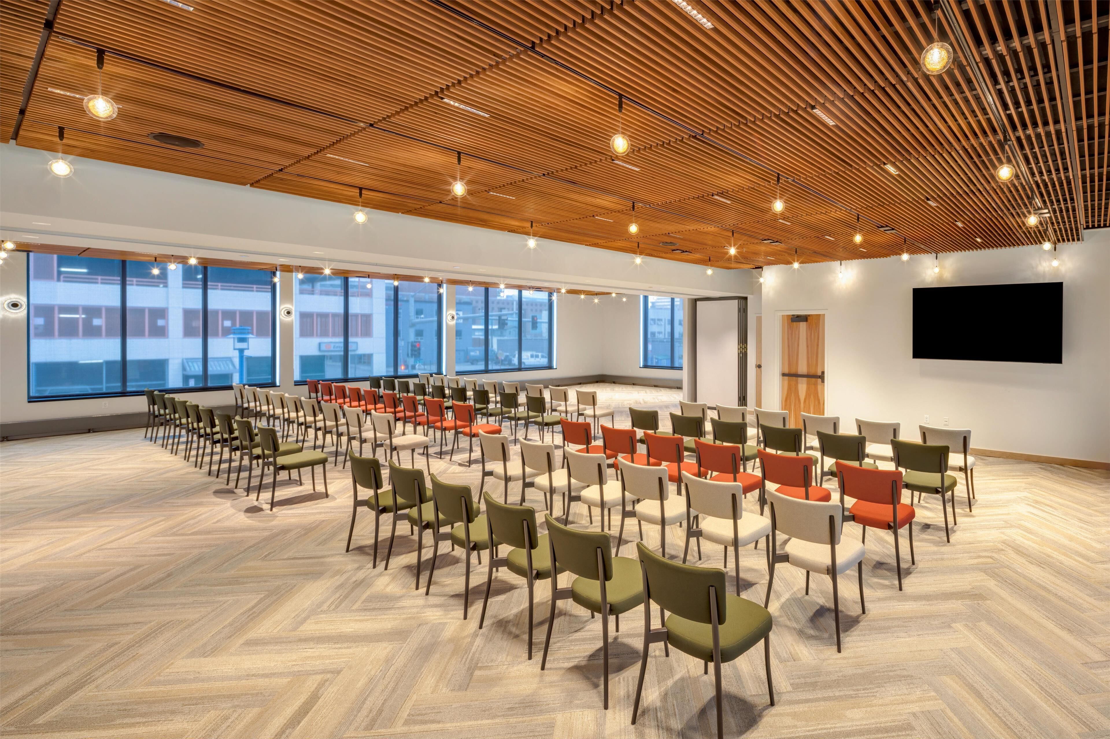 A spacious conference room with rows of chairs, large windows, and a wooden ceiling.