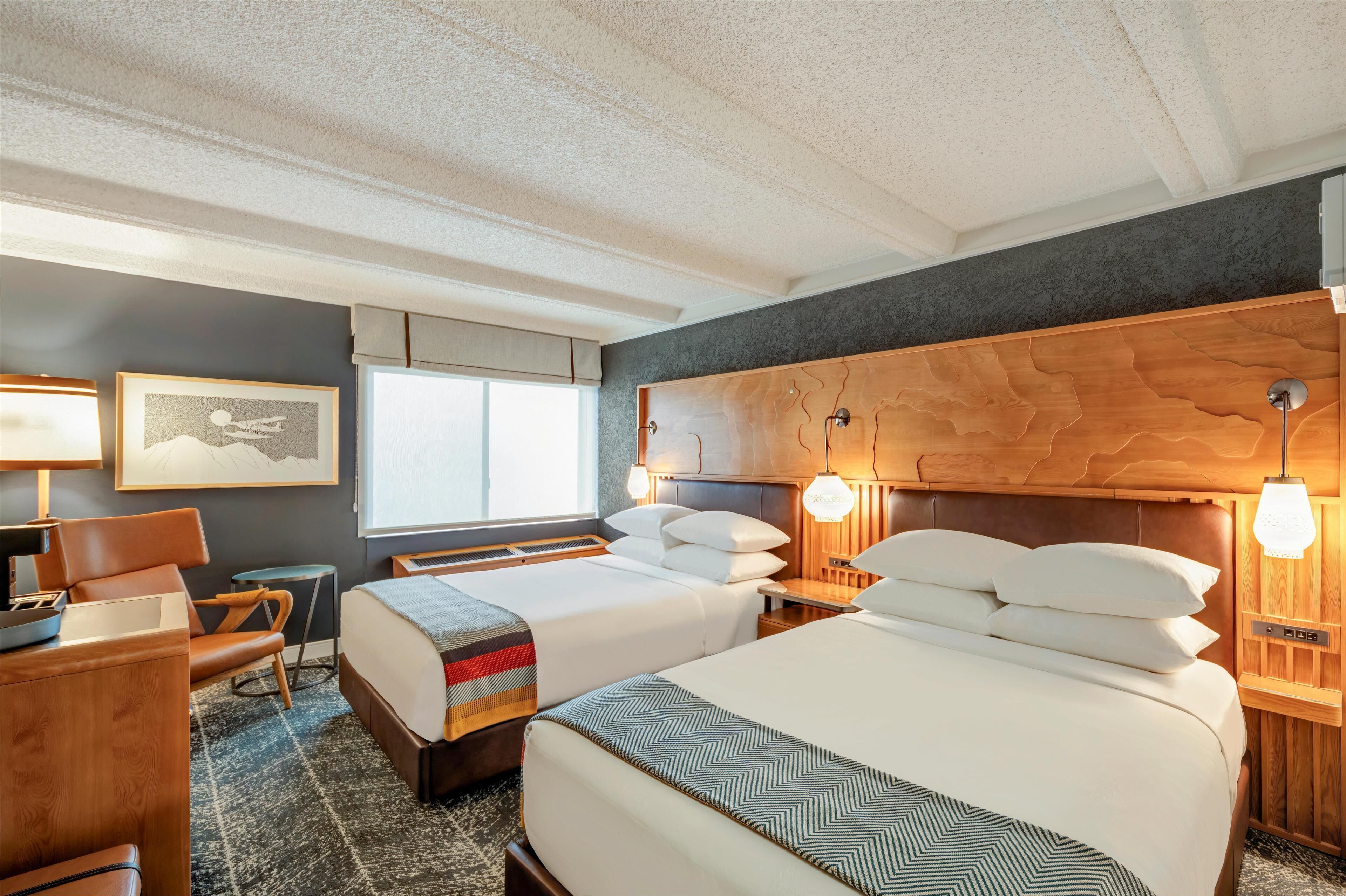 Ein Hotelzimmer mit zwei Betten, einem Schreibtisch, einem Stuhl, einer Lampe und einem Fenster.