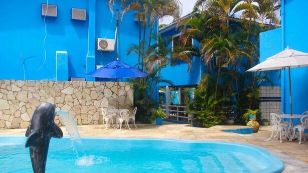 A swimming pool with a dolphin statue, surrounded by a stone wall and palm trees. - Morada Azul (Ipojuca)