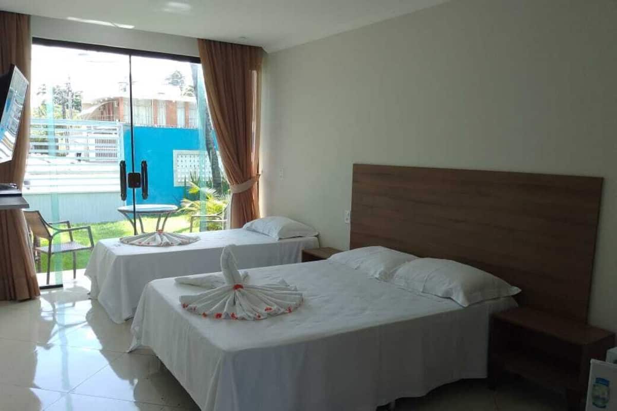 Habitació d'hotel amb un llit gran, un altre més petit, un escriptori i una cadira. Hi ha una televisió penjada a la paret i una finestra amb cortines.