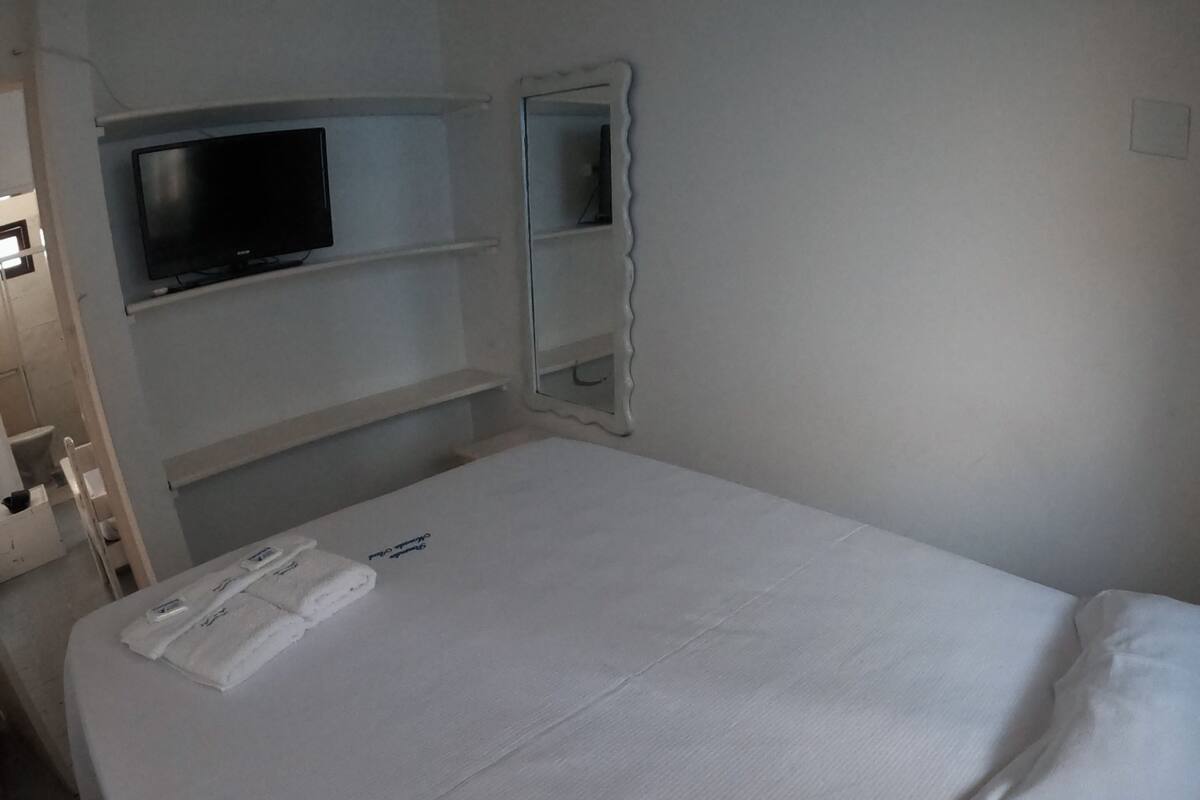 Un llit ben fet amb un edredó blanc i coixins, un televisor de pantalla plana muntat a la paret i una petita estant amb un mirall.