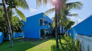 A modern blue building with a two-story structure, surrounded by a well-maintained lawn and palm trees. - Morada Azul (Ipojuca)