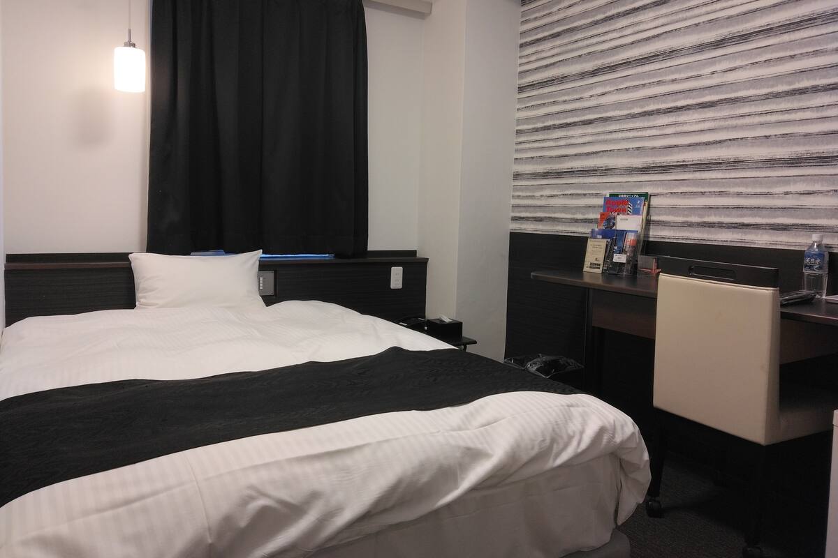 Une chambre d’hôtel avec un lit, un bureau et une fenêtre équipée de stores.