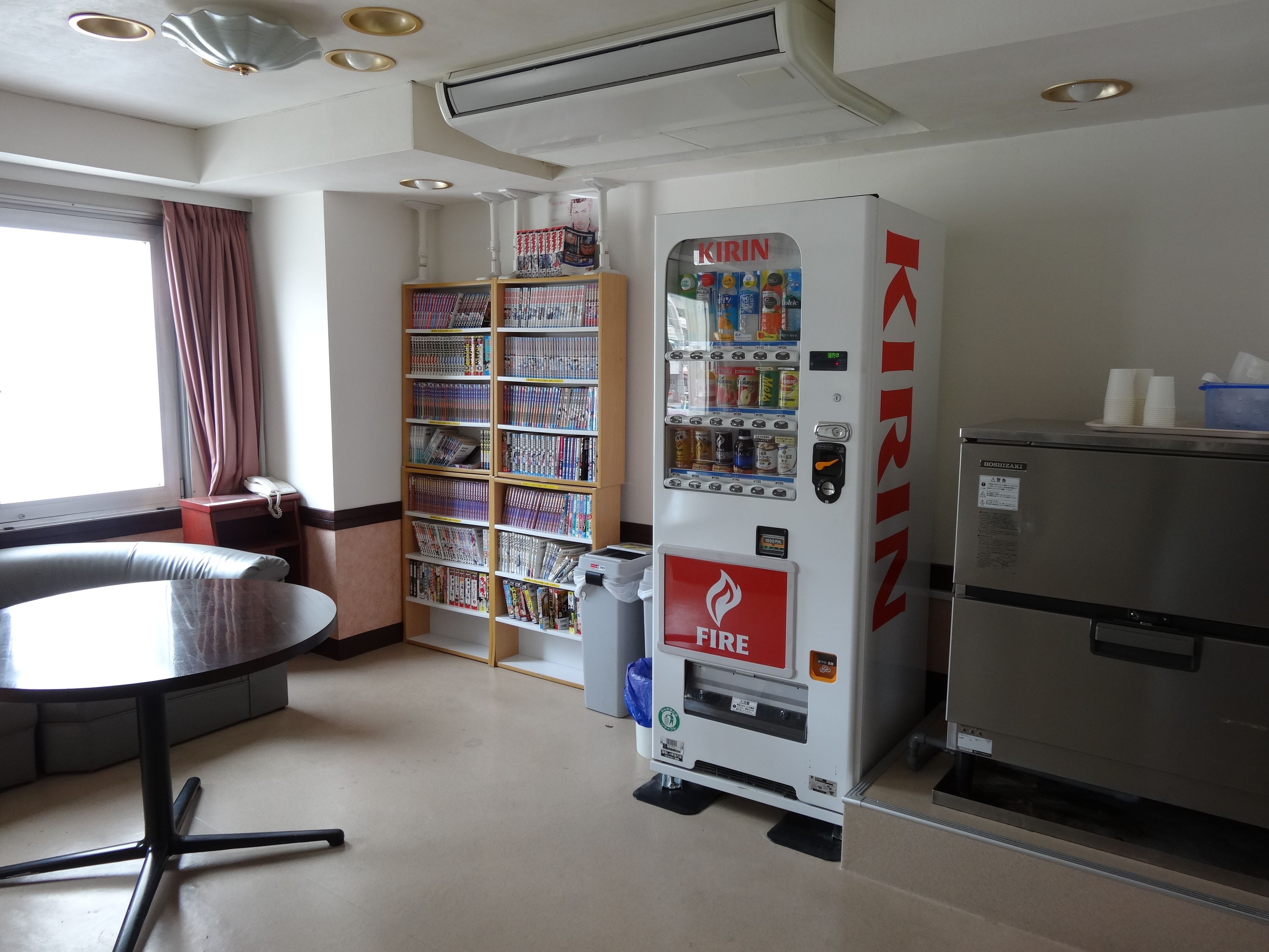 Une chambre d’hôtel équipée d’un mini-bar, d’un distributeur automatique, d’une bibliothèque et d’une fenêtre avec des rideaux.