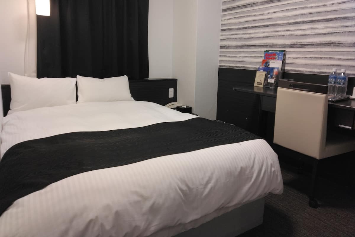 Une chambre d’hôtel avec un grand lit, un bureau et une fenêtre avec des stores.
