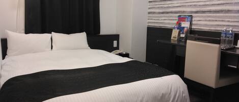 Une chambre d’hôtel avec un grand lit, un bureau et une fenêtre avec des stores.