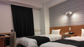 Hotelkamer met twee bedden, een bureau, een stoel, een telefoon en een wandlamp.