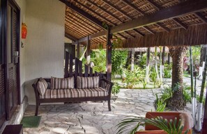 A stone-floored patio with a wooden bench and a thatched roof structure. - Pousada Recanto da Coruja (Ipojuca)