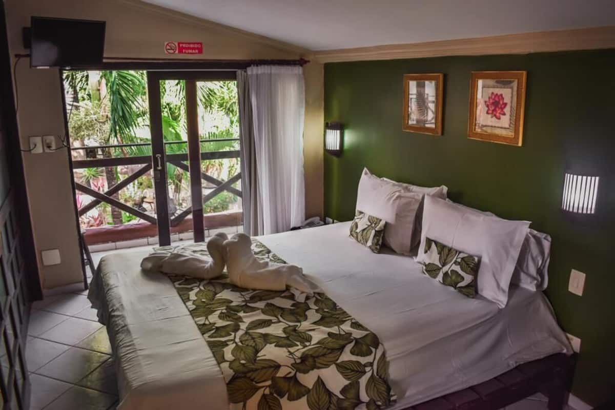 A hotel room with a bed, a view of greenery outside, and a sign indicating no smoking.