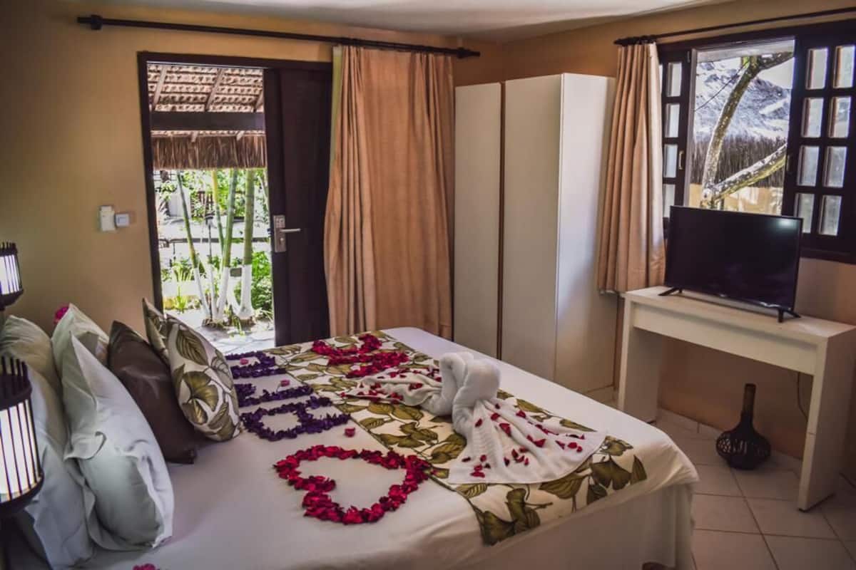 A hotel room with a bed, a TV, a desk, and a view of mountains through the window.