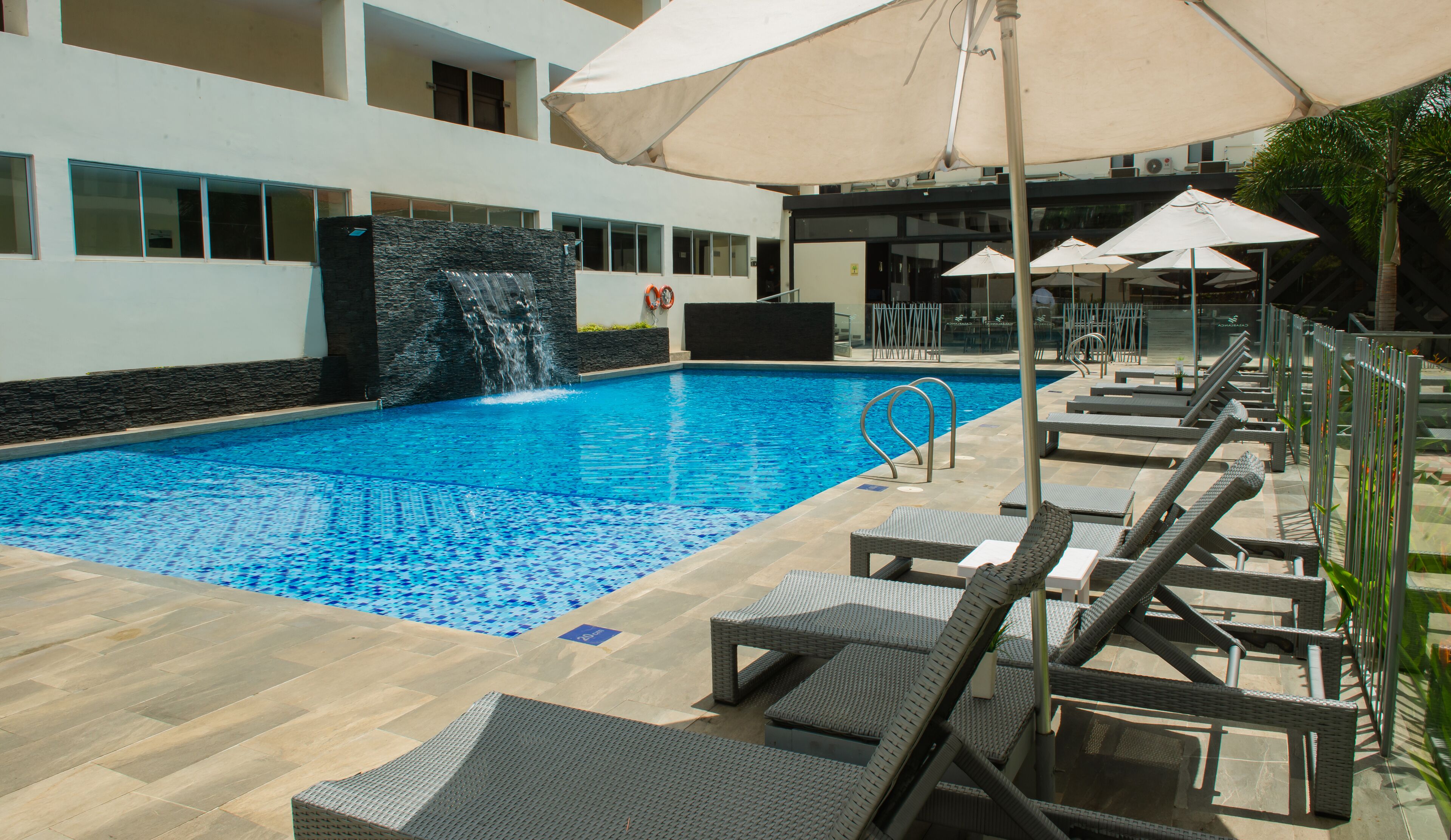 A swimming pool with a waterfall feature, surrounded by lounge chairs and umbrellas.