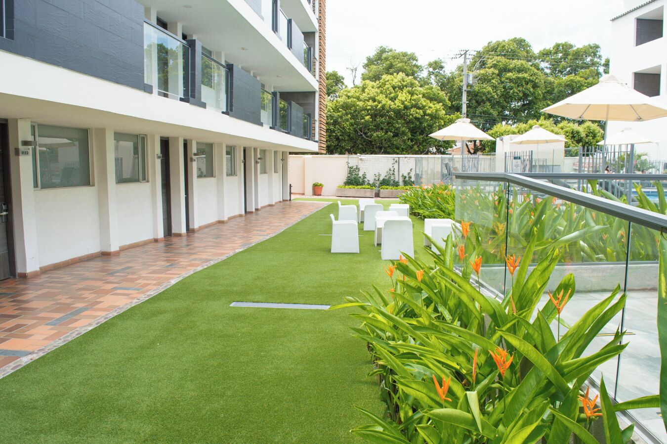 Un edificio moderno con techo plano, un sendero pavimentado y un pequeño jardín con sillas blancas.