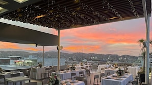 A rooftop restaurant with tables set for dining, overlooking a cityscape at sunset. - Hotel Casa Blanca (San José de Cúcuta)