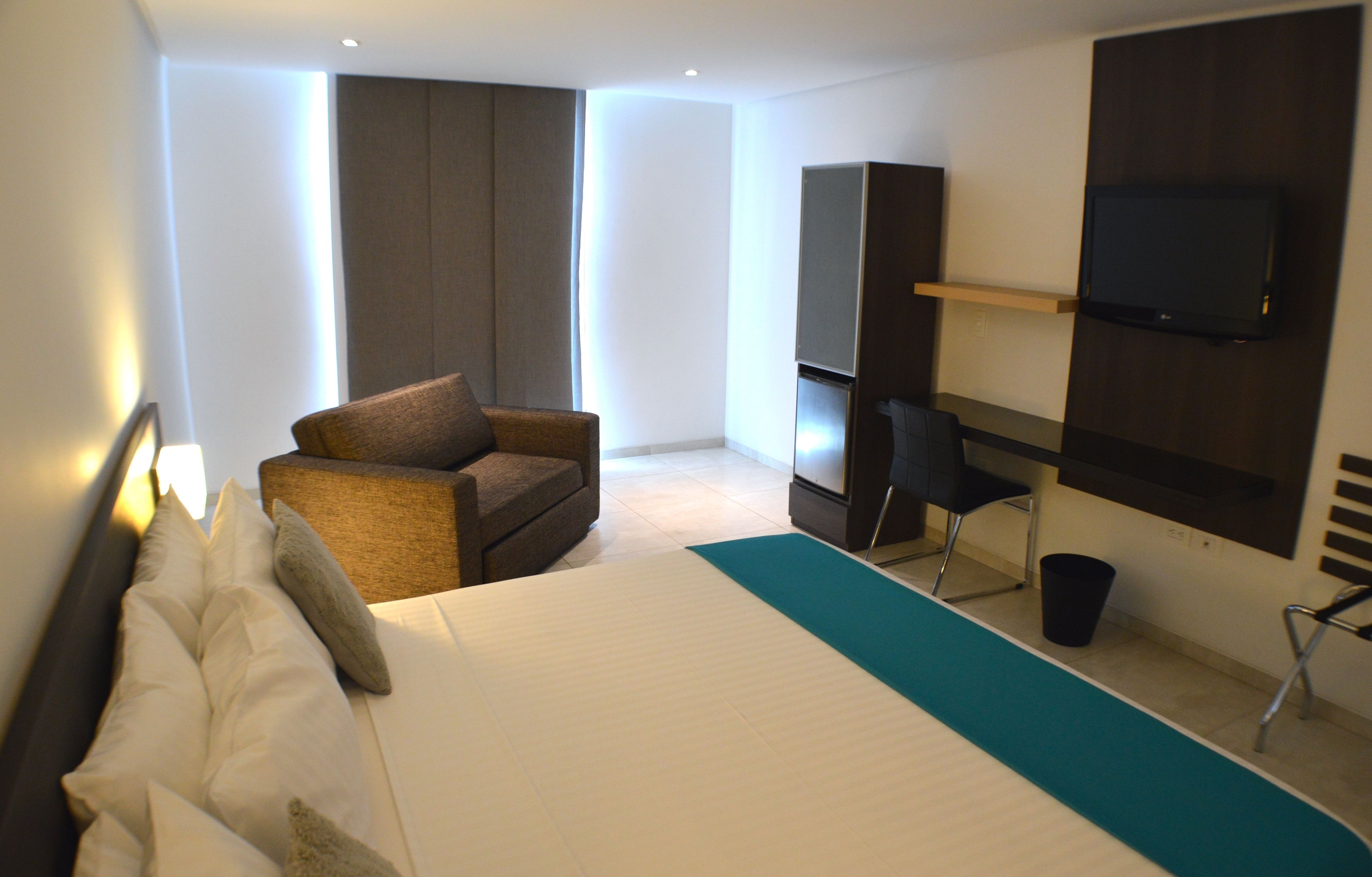 Quarto de hotel com uma cama grande, um sofá, uma escrivaninha, uma TV e televisão na parede.