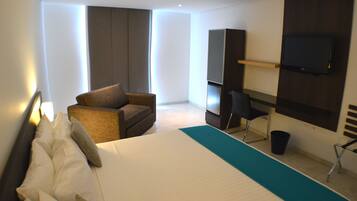 Quarto de hotel com uma cama grande, um sofá, uma escrivaninha, uma TV e televisão na parede.