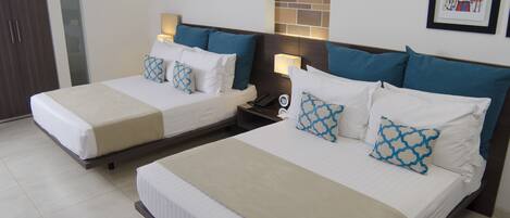 Een hotelkamer met twee bedden, elk voorzien van witte lakens en blauw gestreepte kussens. Er staan nachtlampjes en een klein tafeltje met een telefoon.